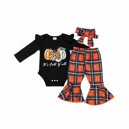 A baby girl's fall-themed two-piece outfit set laid flat on a gray wood plank floor. The set includes a black long-sleeve bodysuit with a pumpkin and leopard print graphic and the text 'It's Fall If u like', paired with orange, navy, and white plaid pants and a matching plaid bow headband.