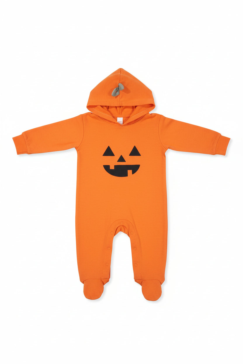 An orange long-sleeve baby bodysuit or pajama set laid flat on a dark wood floor, featuring a black pumpkin face graphic on the chest and a matching hood with a gray zipper.